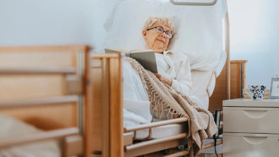 femme âgée allongée sur un lit d'hôpital, en train de lire un livre