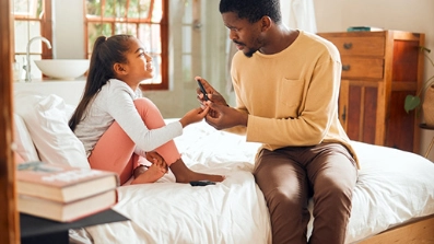 Un père et sa fille discutent assis au bord d'un lit.