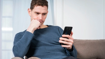 Homme seul sur un canapé, pensif, absorbé par son téléphone.