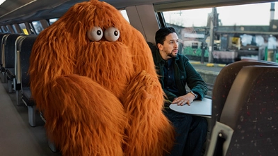 Un homme pensif assis dans un train accompagné d’un monstre poilu aux grands yeux
