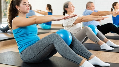 Participants d'un cours de Pilates utilisant des ballons de fitness pour améliorer leur posture et équilibre dans un environnement lumineux.