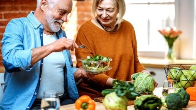 Un couple de seniors souriants prépare un repas sain dans leur cuisine.