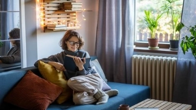 Femme habillée chaudement confortablement assise dans son salon avec un livre.