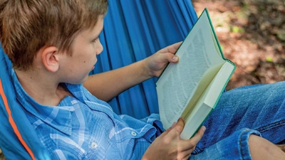 Un enfant lit assis dans un hamac.