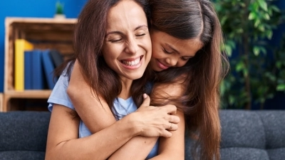 Une petite fille serre sa maman dans ses bras. Elle sourient toutes les deux.