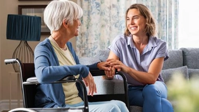 Une femme adulte souriante rend visite à sa mère âgée en fauteuil roulant.