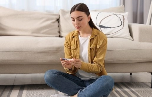 Jeune femme assise sur le sol, tenant un test de grossesse, avec une expression concentrée, dans un salon lumineux.