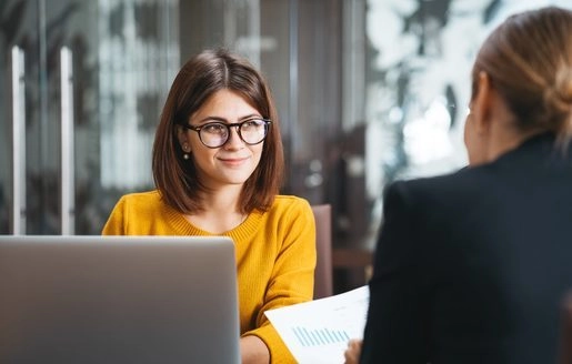 Femme en pull jaune souriant lors d’une réunion, devant un ordinateur.