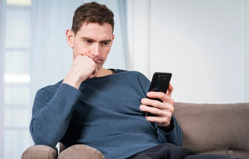 Homme seul sur un canapé, pensif, absorbé par son téléphone.