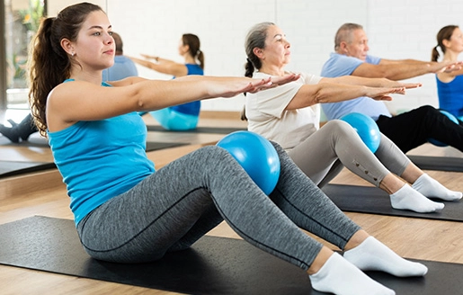 Participants d'un cours de Pilates utilisant des ballons de fitness pour améliorer leur posture et équilibre dans un environnement lumineux.