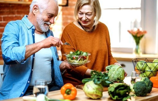 Un couple de seniors souriants prépare un repas sain dans leur cuisine.