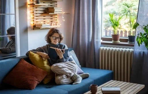 Femme habillée chaudement confortablement assise dans son salon avec un livre.