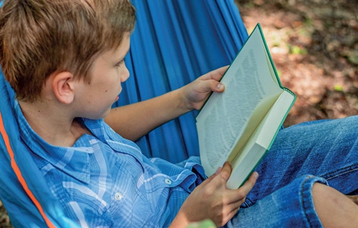 Un enfant lit assis dans un hamac.