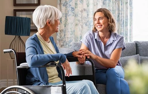 Une femme adulte souriante rend visite à sa mère âgée en fauteuil roulant.