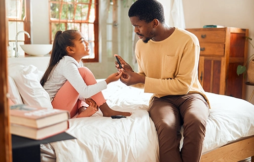 Un père et sa fille discutent assis au bord d'un lit.