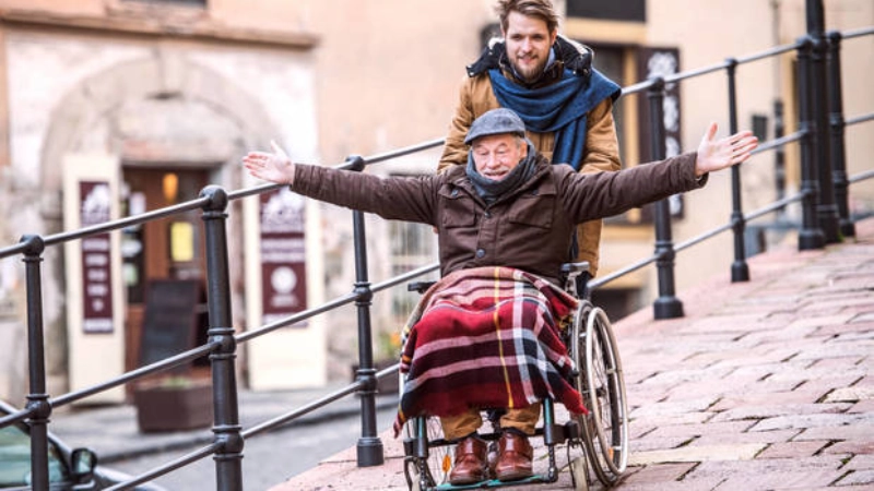 Aidant accompagnant une personne en fauteuil roulant visiblement heureuse.