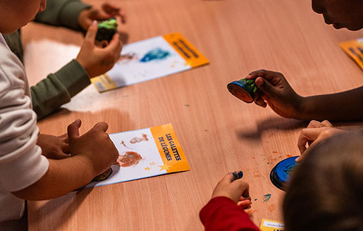 Enfants autour d’une table, tamponnant une feuille de papier avec des pièces de légumes imbibés de peinture.