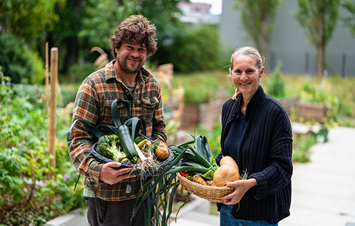 Portrait d’un jardinier et d’une dame portant chacun un panier de légumes fraîchement cueillis.