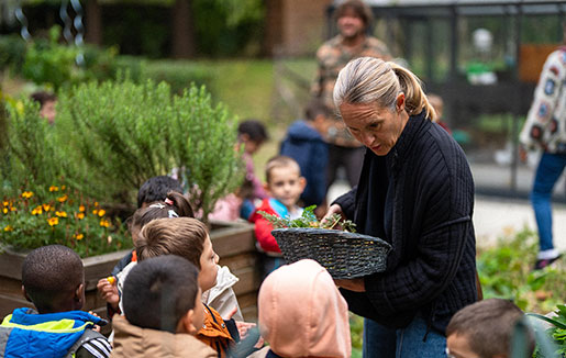 Une dame tenant un panier de légume en présence de jeunes enfants.